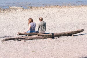 2 Menschen sitzen am Strand auf einem Baum und reden miteinander